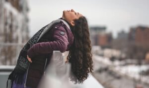 A woman enjoying a peaceful moment outside in winter attire, against a snowy urban backdrop.