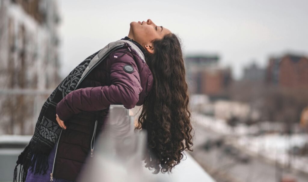 A woman enjoying a peaceful moment outside in winter attire, against a snowy urban backdrop.